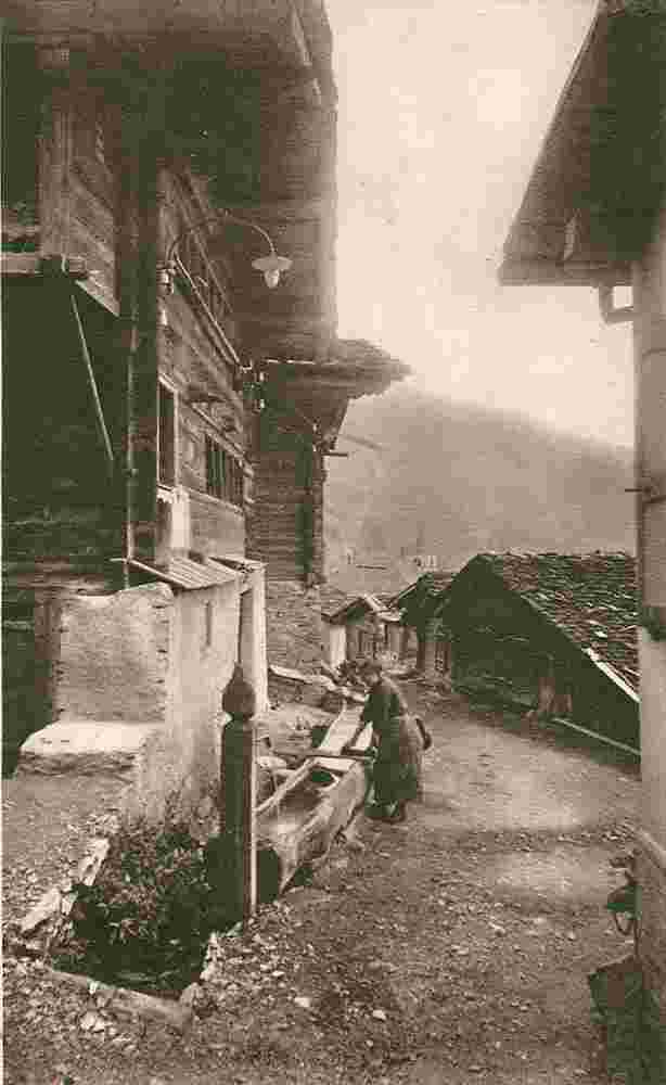 Inden. Frau wäscht Kleider am Dorfbrunnen um 1913